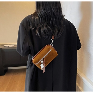 Brown suede crossbody bag worn on a black blazer with silver robot charm detail