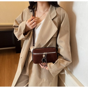 Detail shot of brown suede crossbody bag featuring a silver robot pendant and metal zipper