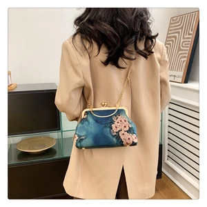 Detail of elegant navy blue floral frame bag with gold metal handle and chain strap