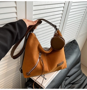 Brown suede hobo bag with zipper detail and hanging coin purse against white shutters