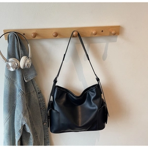 Detailed view of black PU leather shoulder bag with side pockets on a wooden hanger