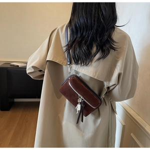 Detail view of brown suede crossbody bag with metal robot pendant on a beige trench coat