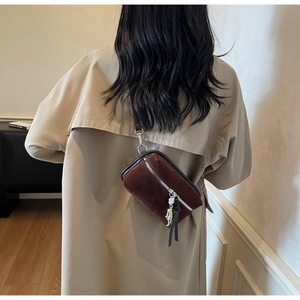 Rear view of brown suede crossbody bag with astronaut pendant on a beige trench coat