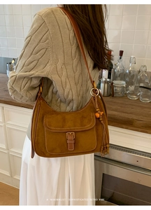 Brown suede crescent bag detail with leather shoulder strap and decorative tassels