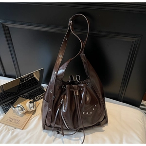 Detail view of brown glossy bucket bag with silver zippers, rivets and leather texture