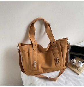Detail of camel tote bag with metal rivets, side pockets, and adjustable nylon shoulder strap
