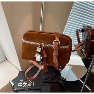 Detail of vintage brown suede crossbody bag with a silver robot charm and zipper texture