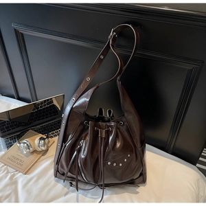 Detail of dark brown glossy bucket bag featuring biker-style silver zippers and eyelet straps