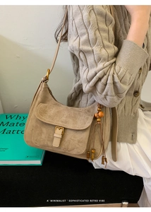 Detail of khaki suede shoulder bag featuring a gold buckle and wooden bead tassel