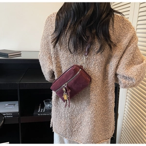Detail of burgundy suede crossbody bag with long tassels and a metallic robot charm