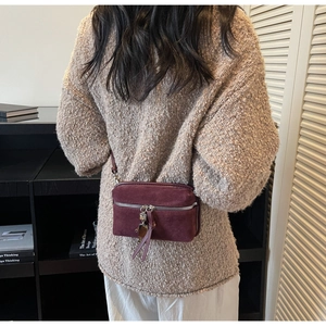 Vue détaillée d'un sac bandoulière en daim bordeaux porté sur un pull en maille beige