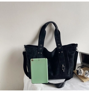 Black matte tote bag detail with metal eyelets, rivets, and a laptop for size reference