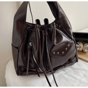 Detail of dark brown glossy bucket bag with silver zippers, rivets and leather texture