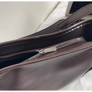 Detailed macro view of smooth dark brown leather texture and silver zipper on tote bag