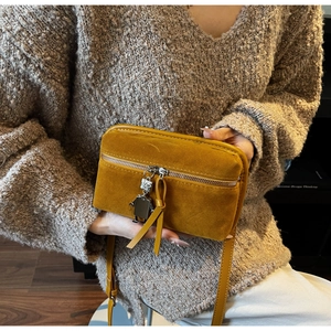 Close-up of mustard yellow suede crossbody bag with robot charm and leather fringe detail