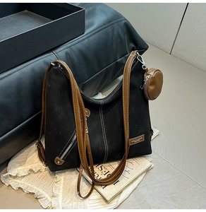 Detail of black suede tote bag with brown leather straps and a round coin purse charm