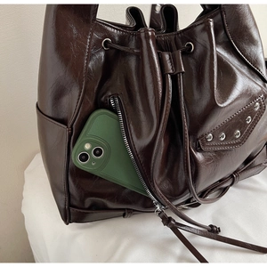 Detail of dark brown glossy leather bucket bag with silver studs and side pocket