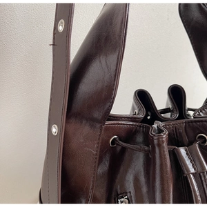 Detail of dark brown oil-wax leather bucket bag with silver eyelets and drawstring closure