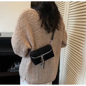 Close-up of black suede crossbody bag with silver robot charm on a knitted sweater