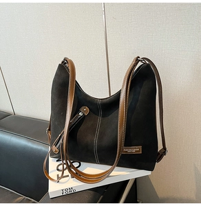 Detail of black tote bag with brown handles, white stitching and side zipper pocket