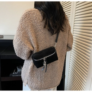 Detail of black suede crossbody bag with silver robot charm and zipper on knit sweater