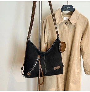 Detail of black suede shoulder bag with brown leather trim and hanging round coin purse
