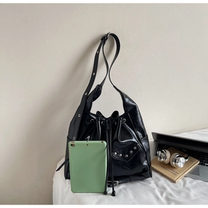 Close-up of black glossy leather bucket bag featuring silver rivet studs and drawstring closure