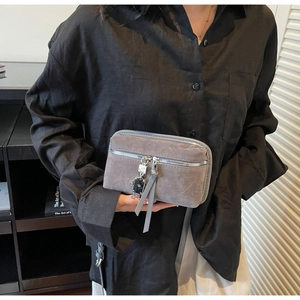 Detail of gray faux suede handbag featuring a silver robot pendant and metal zipper