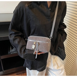 Détail du sac bandoulière en daim gris avec pendentif robot et bandoulière longue