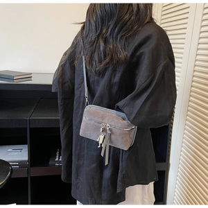 Detail of grey suede crossbody bag with metal robot charm and slim shoulder strap