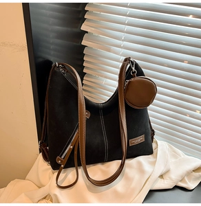 Detail of a large black tote bag with brown leather straps and a small round pouch