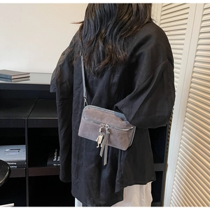 Detail shot of a grey faux suede crossbody bag with robot charm and tassel accents