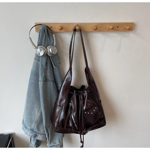 Detail of vintage dark brown leather bucket bag with silver rivets hanging on a wooden hook