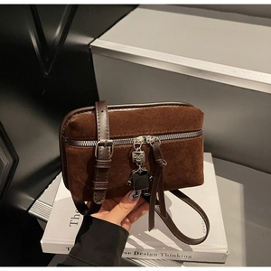 Detail of dark brown suede crossbody bag with metal robot charm on a grey step