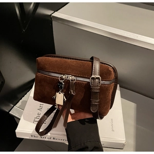 Detail of dark brown suede crossbody bag with silver zipper and robot charm accessory