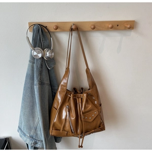 Detail of tan bucket bag featuring drawstring closure with side zipper and metal studs