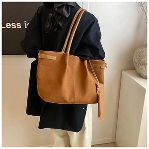 Détail du sac cabas en daim marron avec de longues bandoulières et décoration de pendentif