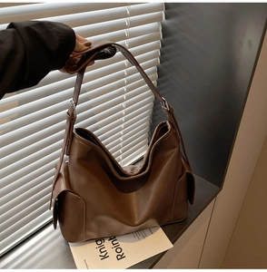 Close-up of brown PU leather tote bag with side flap pockets and wide shoulder strap