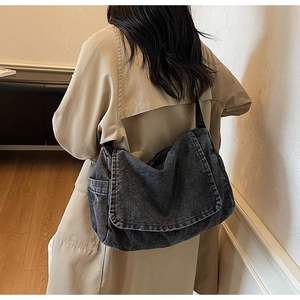 Detail of dark grey washed denim messenger bag showing high capacity and soft texture