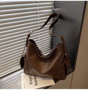 Detail of dark brown matte leather shoulder bag featuring side pockets and silver buckles
