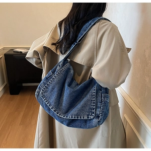Detailed view of dark blue washed denim crossbody bag with contrast white stitching