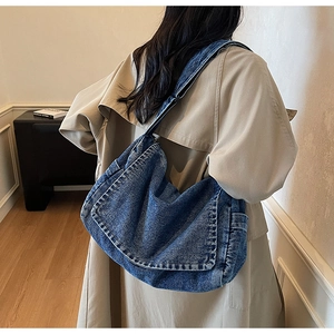 Borsa a tracolla in denim blu con tracolla larga indossata da una modella in interno