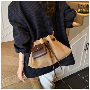 Khaki suede bucket bag with leather detail and drawstring on model in interior setting