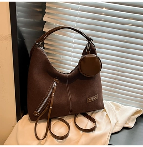 Detail of a brown suede half-moon tote bag with a small round coin purse and leather tag