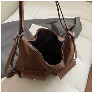 Detail of a dark brown shoulder bag with white contrast stitching and twin flap pockets