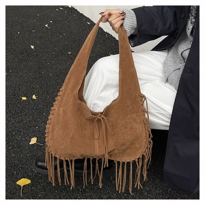 Detail of brown suede hobo bag with long fringes and woven side seams in autumn setting