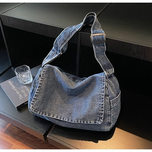 Macro di borsa a tracolla in denim blu lavato con ampia cinghia e patta su uno sfondo scuro