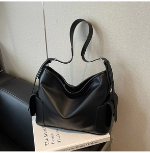 Detail shot of black leather tote bag with flap side pockets on a minimal background