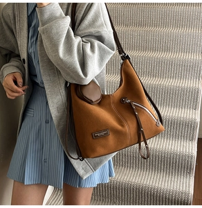 Close-up of brown suede shoulder bag featuring a round pouch and leather strap detail