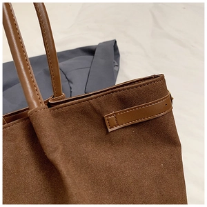 Détails des coutures et boucles dorées sur le cabas en daim marron foncé avec bandoulière